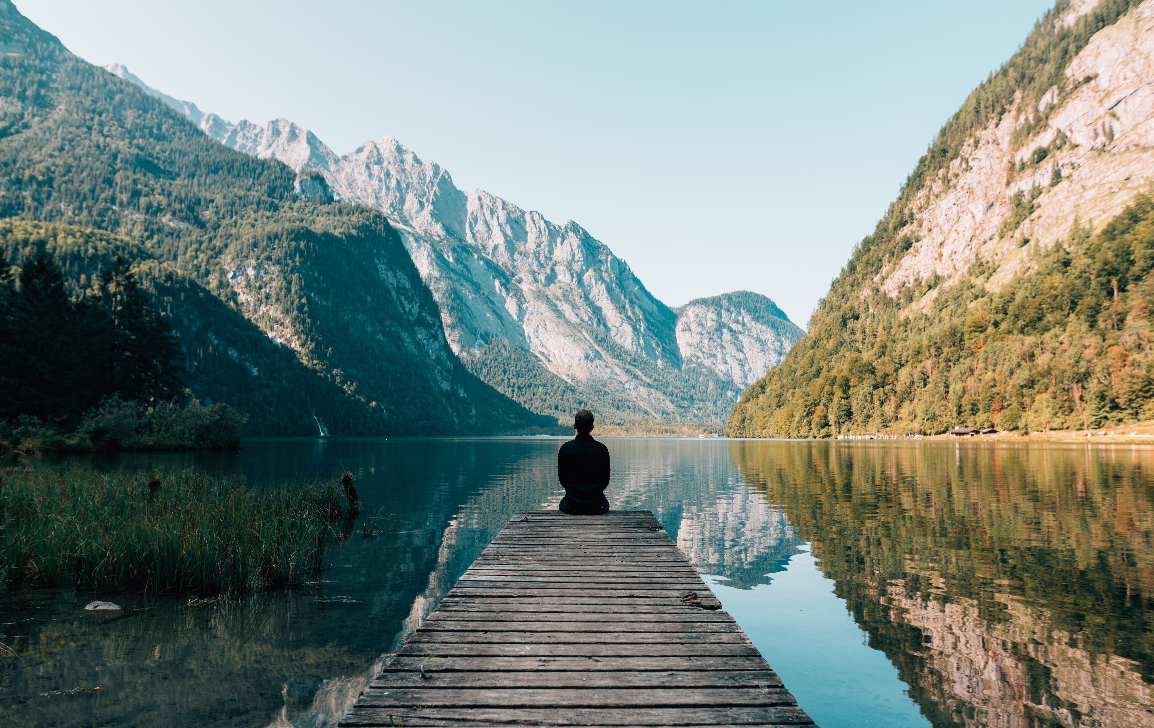 Man sieht einen Mann am See auf einem Steg sitzen und ein schönes Berppanaroma anschauen